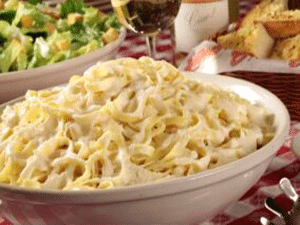 A bowl of alfredo from Buca on a checkered tablecloth with some other Buca dishes